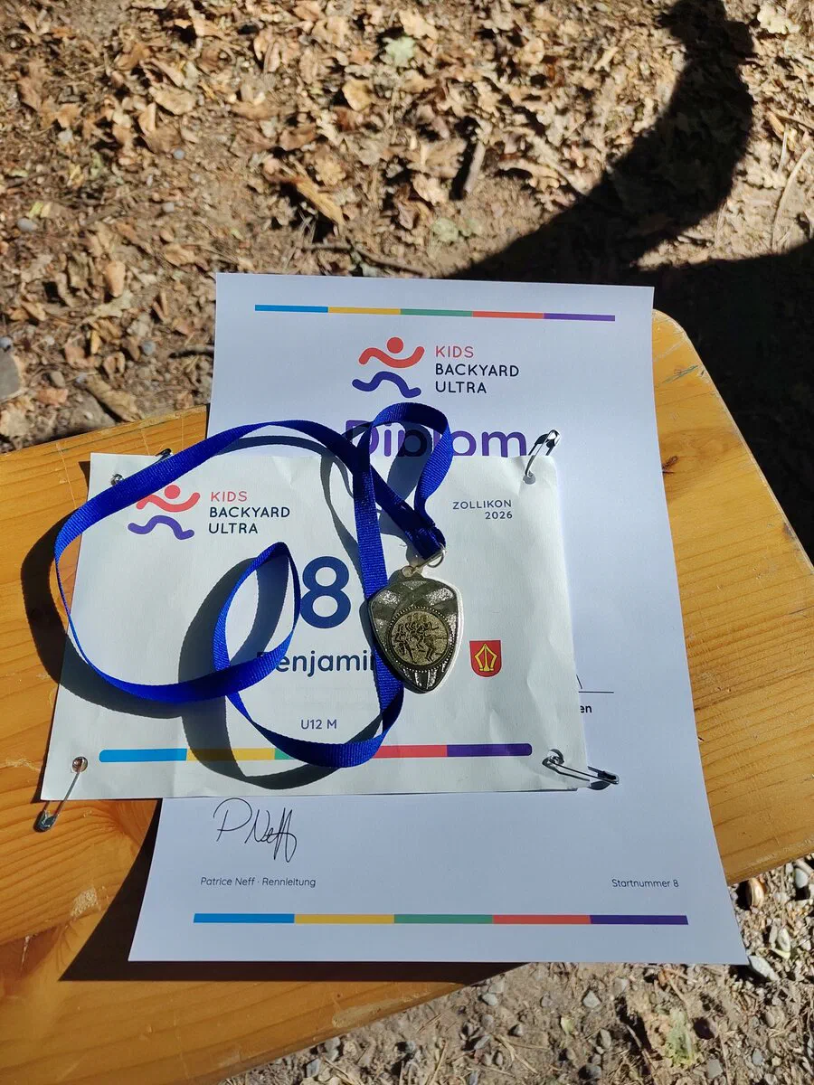 Startnummer, Medaille und Kids-Backyard-Ultra-Diplom auf einer Holzbank