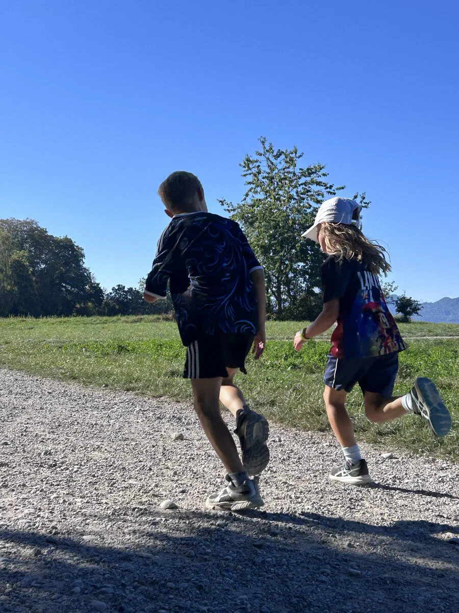 Zwei Kinder laufen gemeinsam auf einem Kiesweg neben einer Wiese